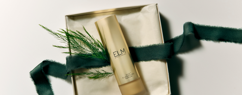 Translation missing: en.Top-down view of A3O™ Elemental Serum bottle in gold with Elm Biosciences logo on a cream gift box tied with dark green ribbon