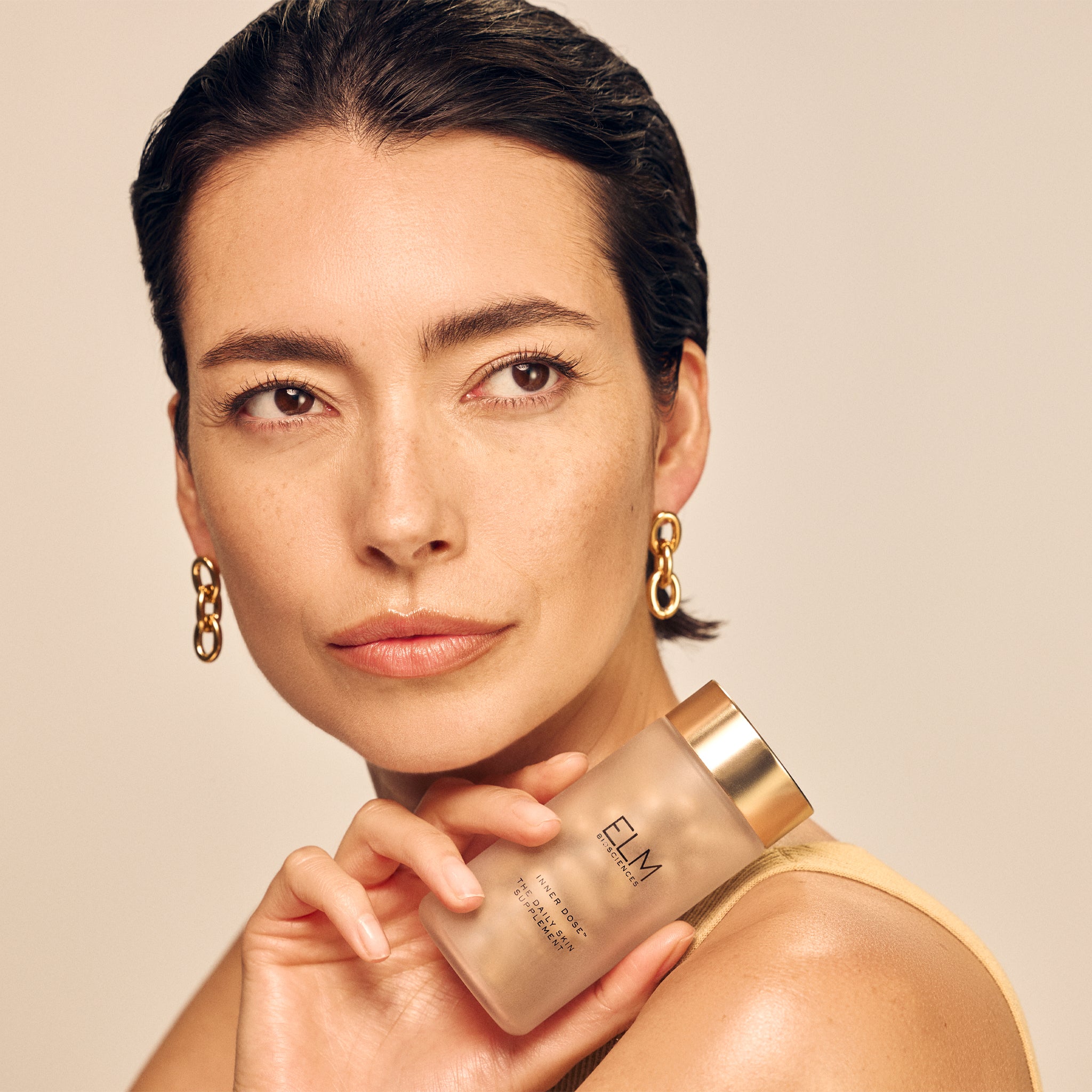 Woman holding a Inner Dose™ Daily Skin Supplement against a beige background